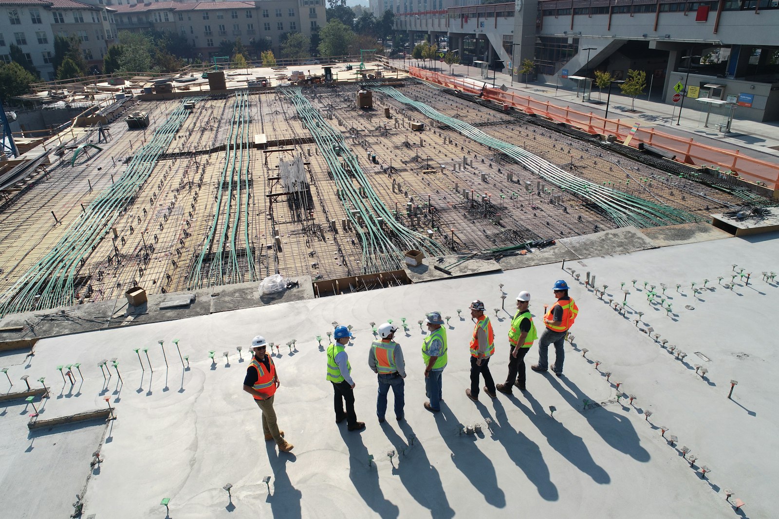 Steel reinforcement laid out across a concrete foundation, with a site team reviewing the work